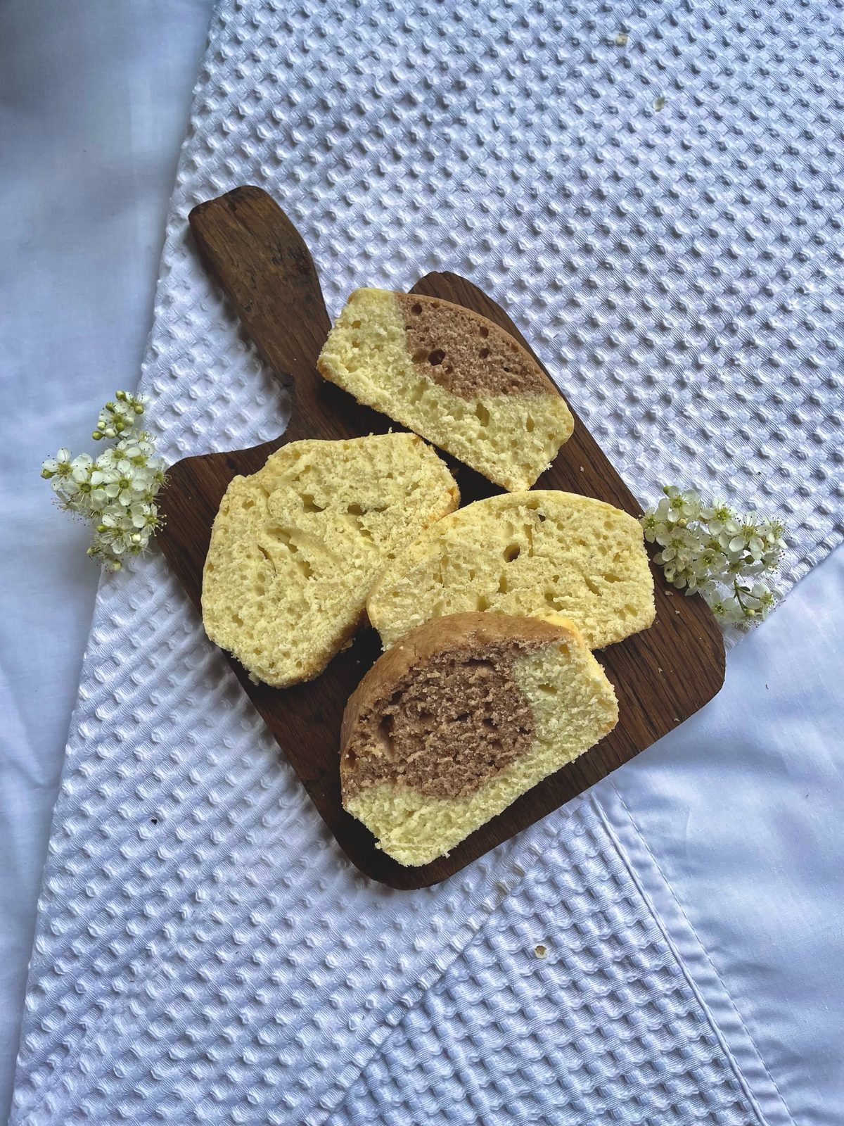 Budín marmolado cortado en rodajas sobre una tabla de madera, con un paño blanco y flores